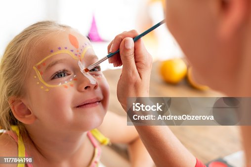 istock Young mother painting daughters face for Halloween party. Halloween or carnival family lifestyle background. Face painting and dressing up. 1177844198