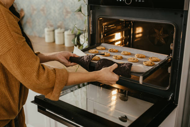 Young mother putting a tray full of cookies in the oven stock photo