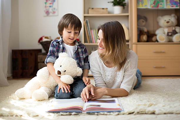Young mother, read a book to her child, boy Young mother, read a book to her child, boy in the living room of their home, rays of sun going through the window teddy ray stock pictures, royalty-free photos & images
