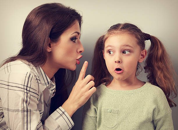 Young mother showing finger the silence sign to her kid stock photo