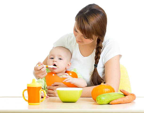young mother spoon feeding her baby boy isolated on white stock photo