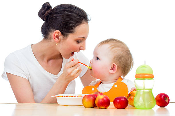 young mother spoon feeding her baby girl stock photo