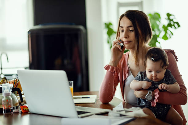 jonge moeder praten op de telefoon tijdens het gebruik van laptop thuis. - working from home stockfoto's en -beelden