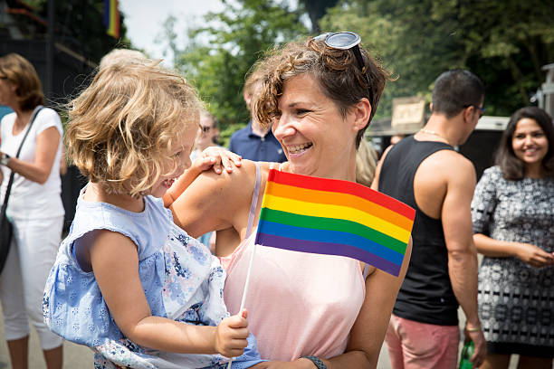 young mother with her daughter waving a rainbow flag Amsterdam, the Netherlands - July 23, 2016: young mother with her daughter in her arms waving a rainbow flag during Pink Saturday celebration in Vondelpark for 2016 Gay Euro Pride lgbtqia culture stock pictures, royalty-free photos & images
