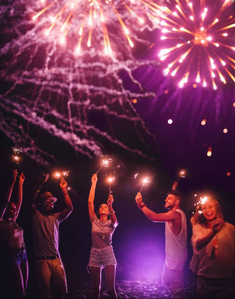 Young multi-ethnic hipster friends celebrating with sparklers and fireworks display Young multi-ethnic hipster friends celebrating Fourth of July with sparklers and a fireworks display firework explosive material stock pictures, royalty-free photos & images