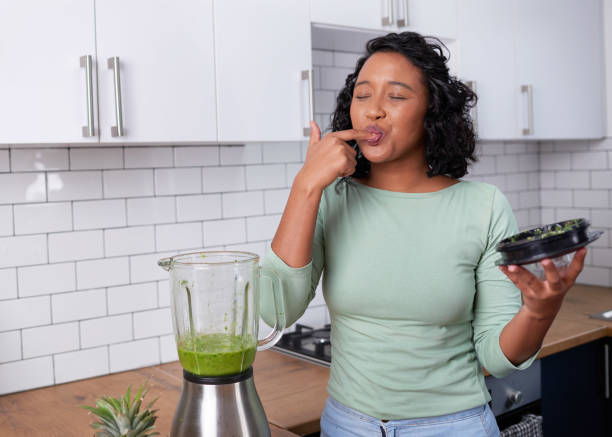 A young multi-ethnic woman tastes her freshly made green smoothie in the kitchen stock photo