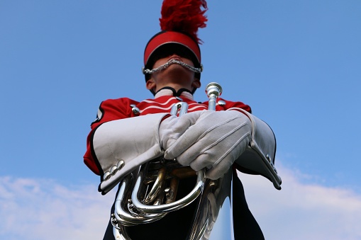 High angle view of young musician in red uniform with marching baritone against blue sky.
