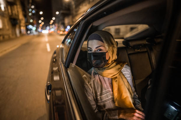 Young muslim woman sitting on back seat at night ride and looking through window stock photo
