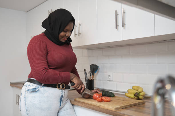 Young muslim woman smiling and cutting vegetables in the kitchen. stock photo
