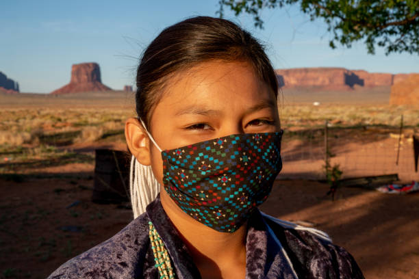 A Young Navajo Girl Wearing A Mask Protecting Her From Covid19, With Monument Valley Behind Her A young Navajo girl wears a mask for protection from Coronavirus stands on her family property in Monument Valley Tribal Park navajo nation covid stock pictures, royalty-free photos & images