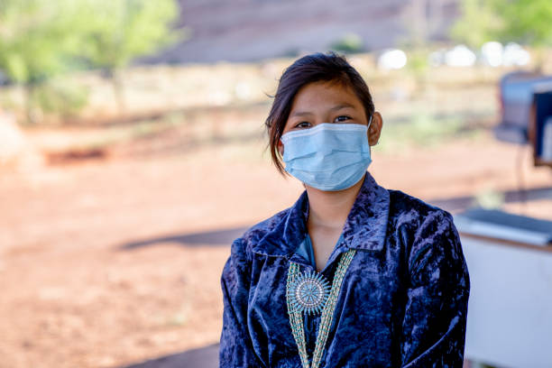 A Young Navajo Girl Wearing A Mask Protecting Her From Covid19, With Monument Valley Behind Her A young Navajo girl wears a mask for protection from Coronavirus stands on her family property in Monument Valley Tribal Park navajo nation covid stock pictures, royalty-free photos & images