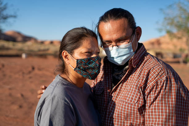 Young Navajo Native American couple Husband Holding Wife and wearing Covid-19 coronavirus masks in Monument Valley Tribal Park at the Arizona/Utah border Young Navajo Native American couple Husband Holding Wife and wearing Covid-19 coronavirus masks in Monument Valley Tribal Park at the Arizona/Utah border navajo nation covid stock pictures, royalty-free photos & images