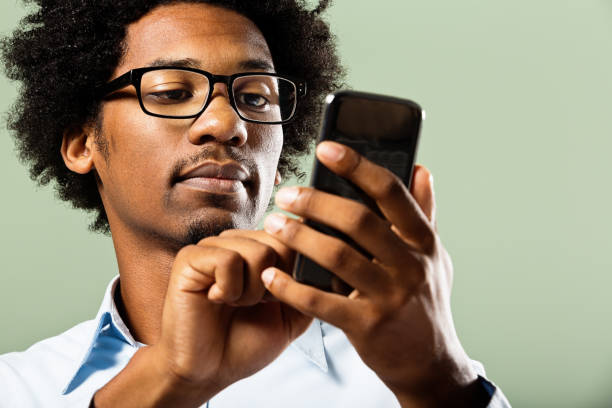Young nerd busy using his cellphone A geeky young black man with afro, goatee and heavy glasses concentrates on using his smartphone. smart phone green background stock pictures, royalty-free photos & images