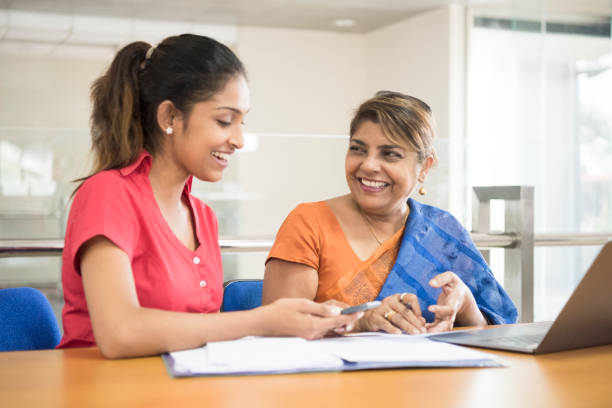 Young office worker and mature businesswoman in meeting, smiling Two Sri Lankan women in office with paperwork, mature woman wearing sari, young woman in pink blouse sri lanka women stock pictures, royalty-free photos & images