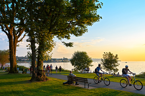 Young couple cycling, others walking or jogging late afternoon and enjoying the sunset at Stanley Park Vancouver, British Columbia, Canada