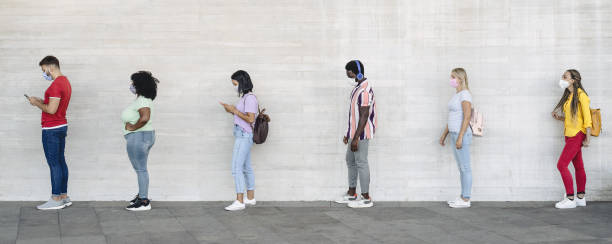 異なる文化や人種の若者が社会的距離を保ちながら店の市場の外で待っている - コロナウイルス拡散防止コンセプト - 行列 ストックフォトと画像