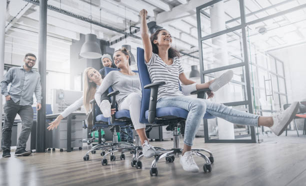 Young people having fun in the office. Happy team. Young cheerful business people dressed in casual clothing are having fun on rowing chairs in a modern office. Happy team concept. happy friday stock pictures, royalty-free photos & images