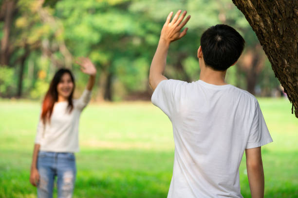 Young people, man and woman greeting or saying goodbye by waving hands in the park.  wave goodbye asian stock pictures, royalty-free photos & images