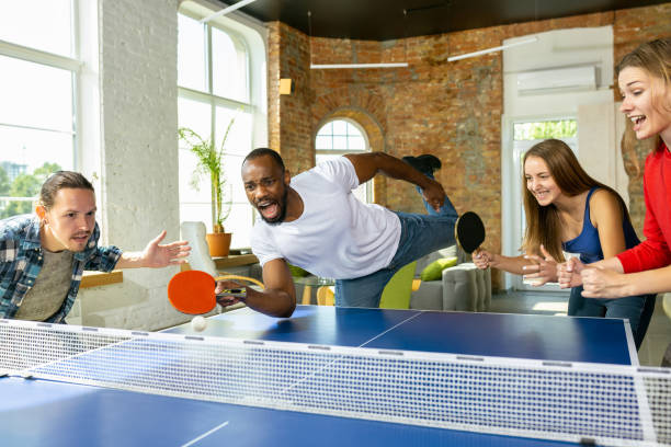 Young people playing table tennis in workplace, having fun Young people playing table tennis in workplace, having fun. Friends in casual clothes play ping pong together at sunny day. Concept of leisure activity, sport, friendship, teambuilding, teamwork. table tennis stock pictures, royalty-free photos & images