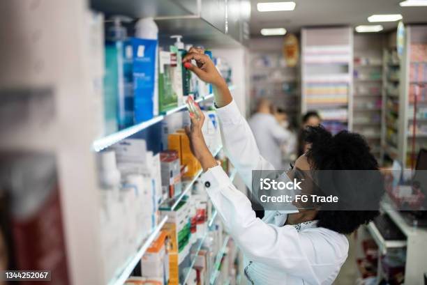 Young pharmacist organizing a shelf at the pharmacy - wearing a face mask