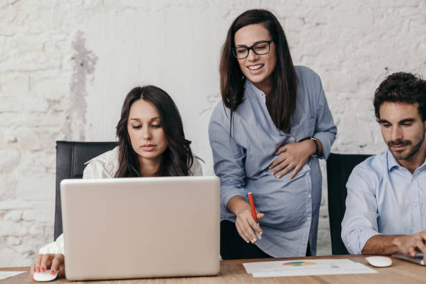 Young pregnant woman at work with his associates in the office while tells them what to do stock photo
