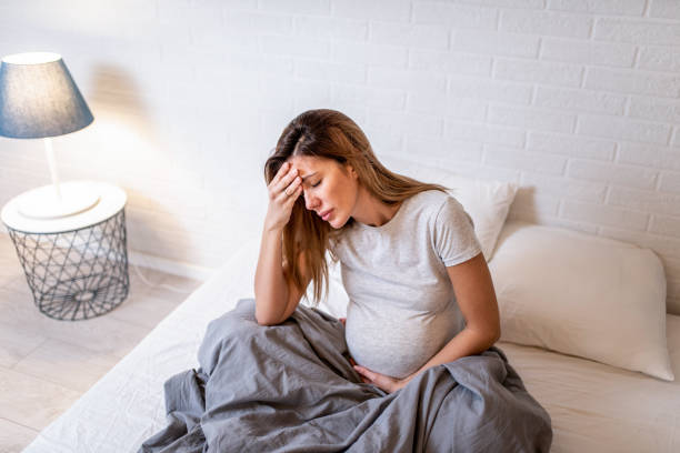 Young pregnant woman experiencing belly pain and headache. stock photo