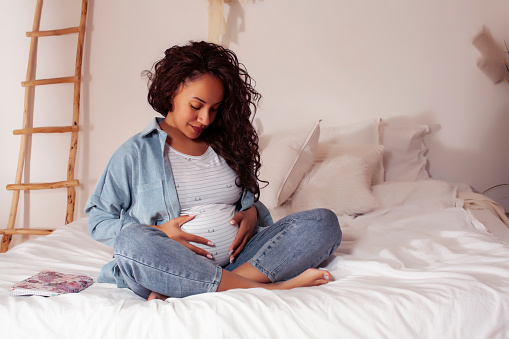 young pretty african american woman pregnant laying in bed, lifestyle people concept close up