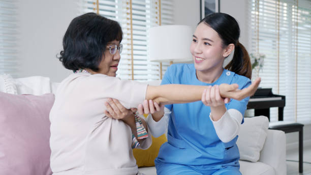 Young senior asia citizen female with scrubs nurse physiotherapy worker at home in rehabilitation therapy service for aging parents. Massage for older care, ache pain joints exercise in old people. stock photo