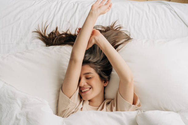Young serene carefree relaxed woman enjoying lying in bed stock photo
