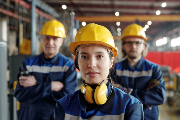 Young serious female worker of large industrial plant or factory in workwear and protective helmet stock photo