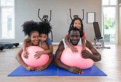 istock Young short curly black hair man and his wife relax on yoga ball while both daughter are on their back. Happy family enjoy holiday together in fitness center. 1399502142