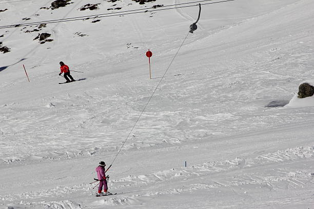 Young Skier at the T-bar lift, Ski Slope Kühtai, Austria - February 6, 2014: Young skier use a T-bar lift direct at the the ski slope. They are a colorful dot in the the white winter landscape. t bar ski lift stock pictures, royalty-free photos & images