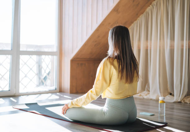 Young slim fitness blonde woman practice morning yoga near the window of home stock photo