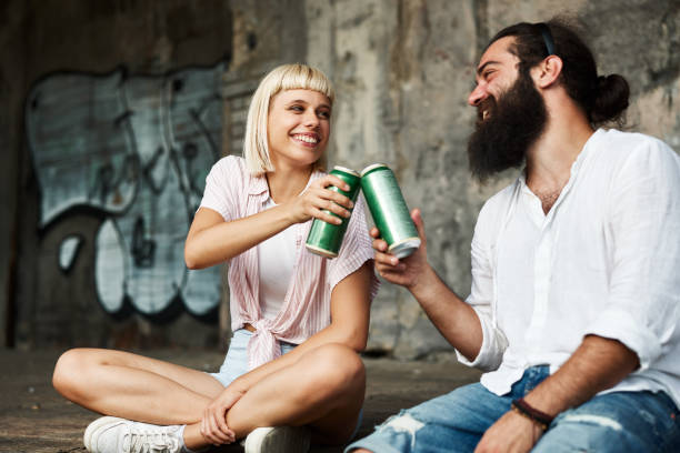 Young smiling couple toasting with beer cans in an urban environment stock photo