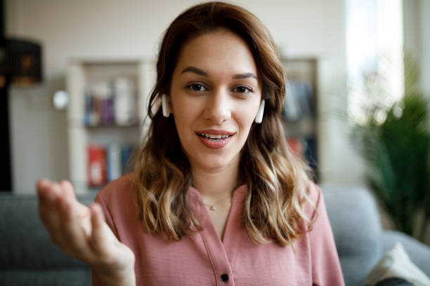 Young smiling woman with bluetooth headphones having video call at home stock photo
