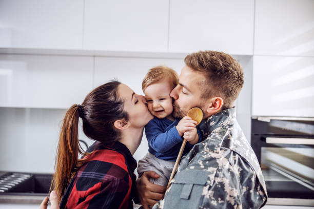 Young soldier arrived home and he is happy with his family. Man and woman kissing their beloved only son.  soldiers returning home stock pictures, royalty-free photos & images
