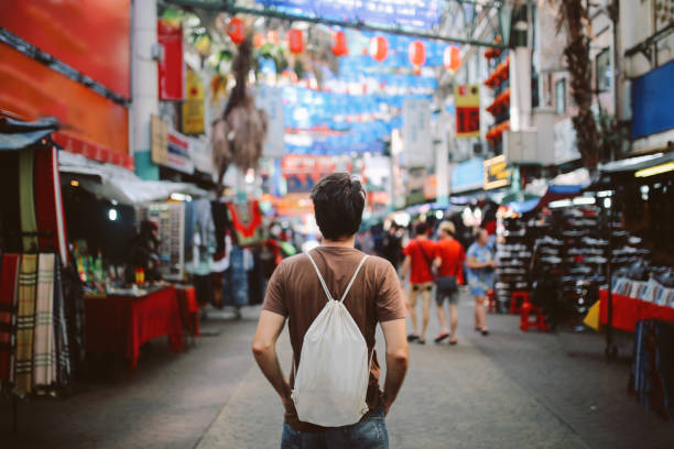 Young solo traveler in Kuala Lumpur Chinatown district Rear view image of a young man, solo traveler, walking in the Chinatown district of Kuala Lumpur, Malaysia. He is wearing a white rucksack, enjoying walking and shopping in Malaysia capital. chinatown kuala lampur stock pictures, royalty-free photos & images