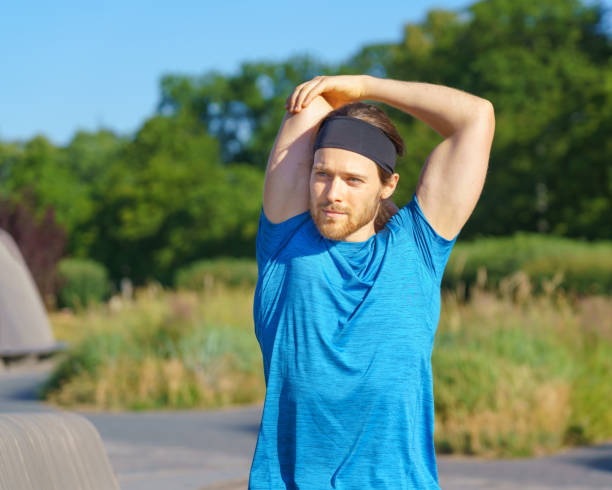 Young sportive man in sportswear warming up in nature in on sunny day stock photo