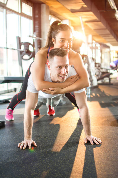 Young sporty couple working out together in gym. Man is doing plank exercise while girl is lying on him. stock photo