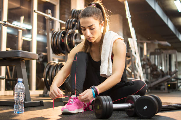 Young sporty woman tying shoes while sitting on floor in gym. Young sporty woman tying shoes while sitting on floor in gym. fitness towel stock pictures, royalty-free photos & images