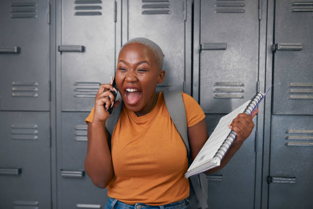A young student screams with happiness on the phone in front of lockers stock photo