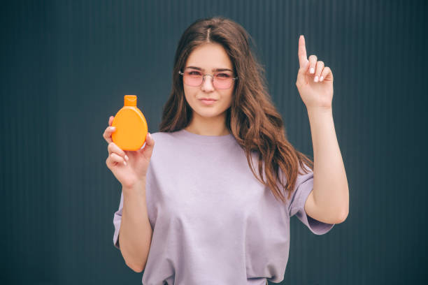 Young stylish trendy woman isolated over grey blue background. Girl holding orange bottle with sunscreen spf face care protection. Stand alone at wall. Young stylish trendy woman isolated over grey blue background. Girl holding orange bottle with sunscreen spf face care protection. Stand alone at wall vlad model photos stock pictures, royalty-free photos & images
