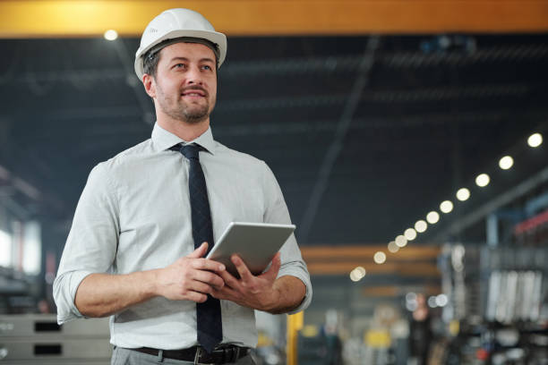 Young successful elegant foreman with touchpad working with data in factory Young successful elegant foreman with touchpad working with data and controling work of industrial machine engineer stock pictures, royalty-free photos & images