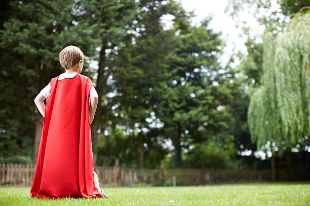 Young superhero searches for danger Rear-view of a little boy in a red cape looking bravely to the horizon cape stock pictures, royalty-free photos & images