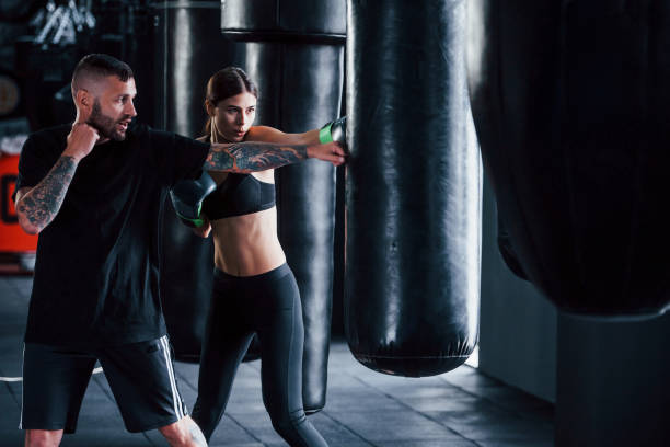 Young tattooed boxing coach teaches young woman in the gym  boxing trainer stock pictures, royalty-free photos & images