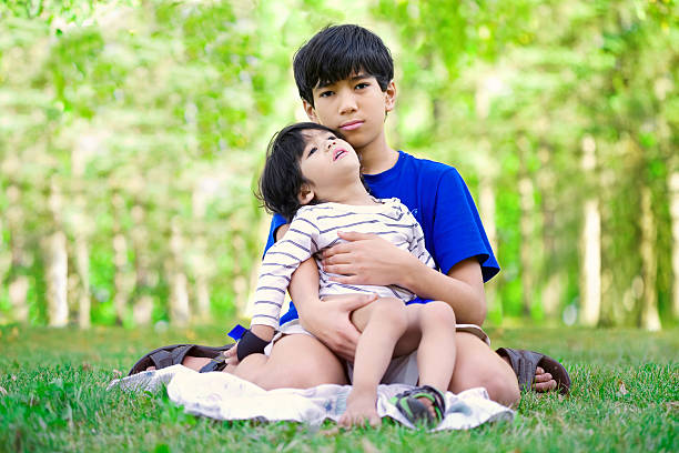 Young teen boy caring for disabled brother Young teen boy caring for disabled brother, looking up into sky asian cerebral palsy baby stock pictures, royalty-free photos & images