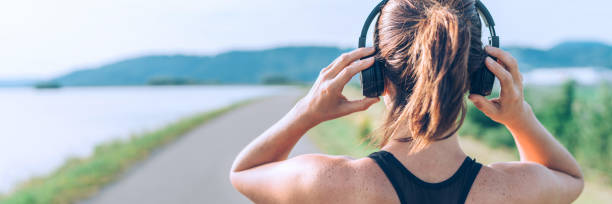 Young teenager girl adjusting wireless headphones before starting jogging and listening to music. Web page header cropping. Young teenager girl adjusting wireless headphones before starting jogging and listening to music. Web page header cropping. active listening stock pictures, royalty-free photos & images