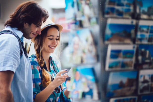 Young tourists buying postcards from souvenir shop Young couple looking at postcards at souvenir shop during their European holidays souvenir stock pictures, royalty-free photos & images