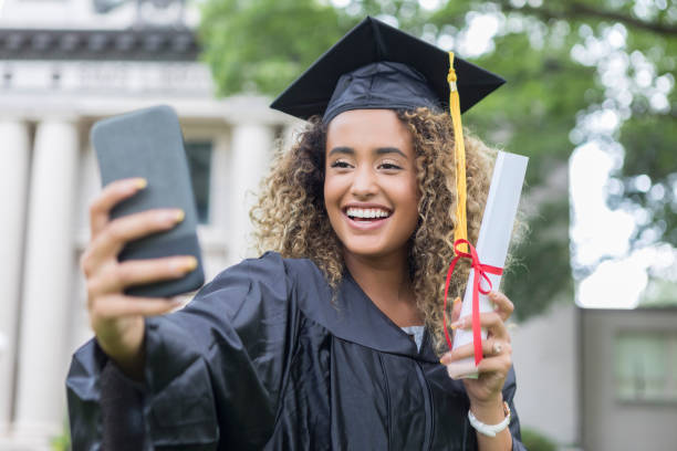 Young university graduate taking selfie Attractive young college graduate smiles while taking selfie. She is holding her diploma. online degree stock pictures, royalty-free photos & images