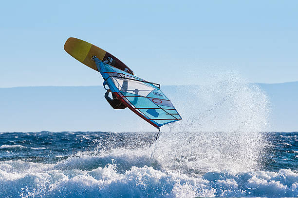 Young Windsurfer Jumping Wave on Windsurf Board Windsurfer riding waves and jumping aquatic sport stock pictures, royalty-free photos & images